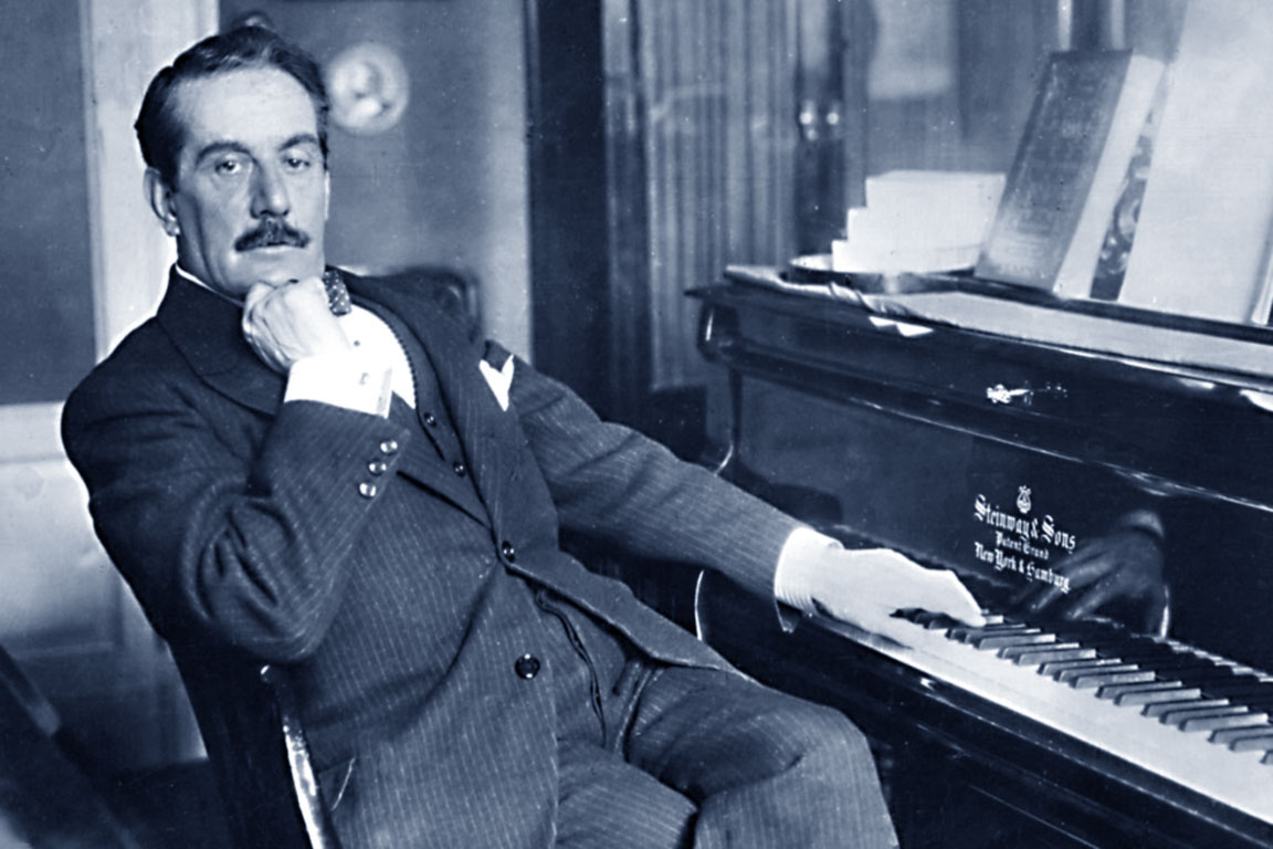 Black and white photo of Giacomo Puccini beside a piano.